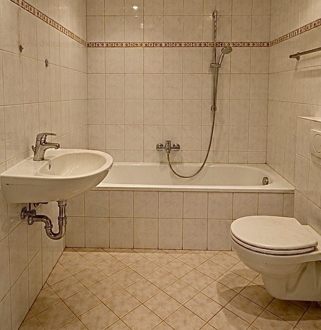 Gefliestes Bad im Altzustand mit Badewanne, Wand-WC und Waschbecken