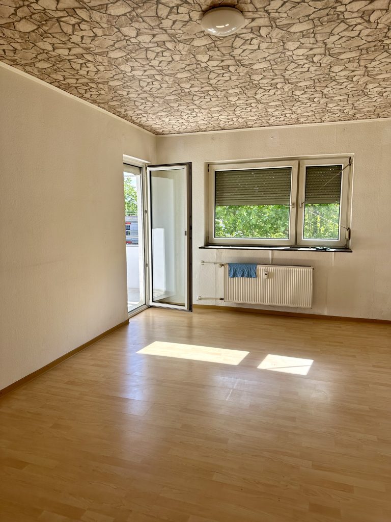 Leeres Wohnzimmer mit offener Balkontür und Rollladenfenster
