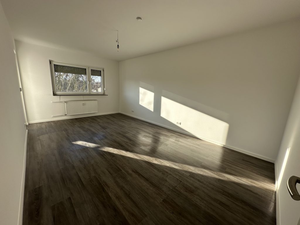 Leeres Wohnzimmer mit dunklem Holzboden und sonnigem Fenster