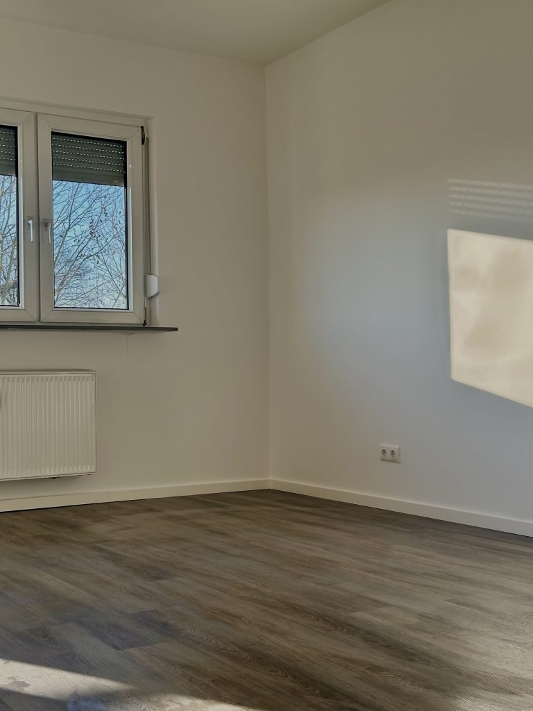 Leerer Raum mit grauem Laminat, Rollladenfenster und Heizkörper