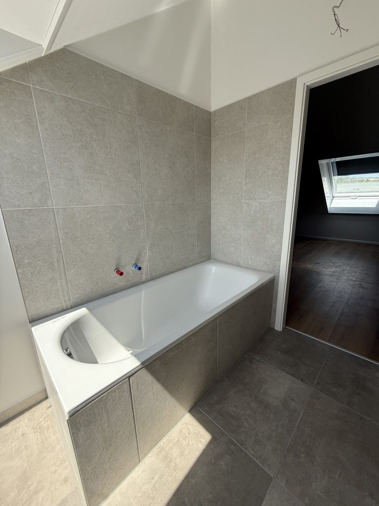 Eingebaute Badewanne mit gefliester Schürze vor Steinoptik-Fliesen