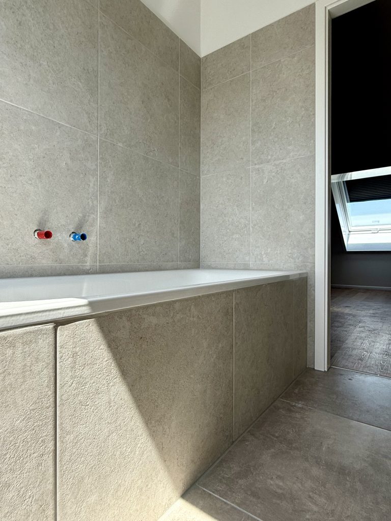Nahaufnahme der roten und blauen Wandanschlüsse über einer gefliesten Badewanne