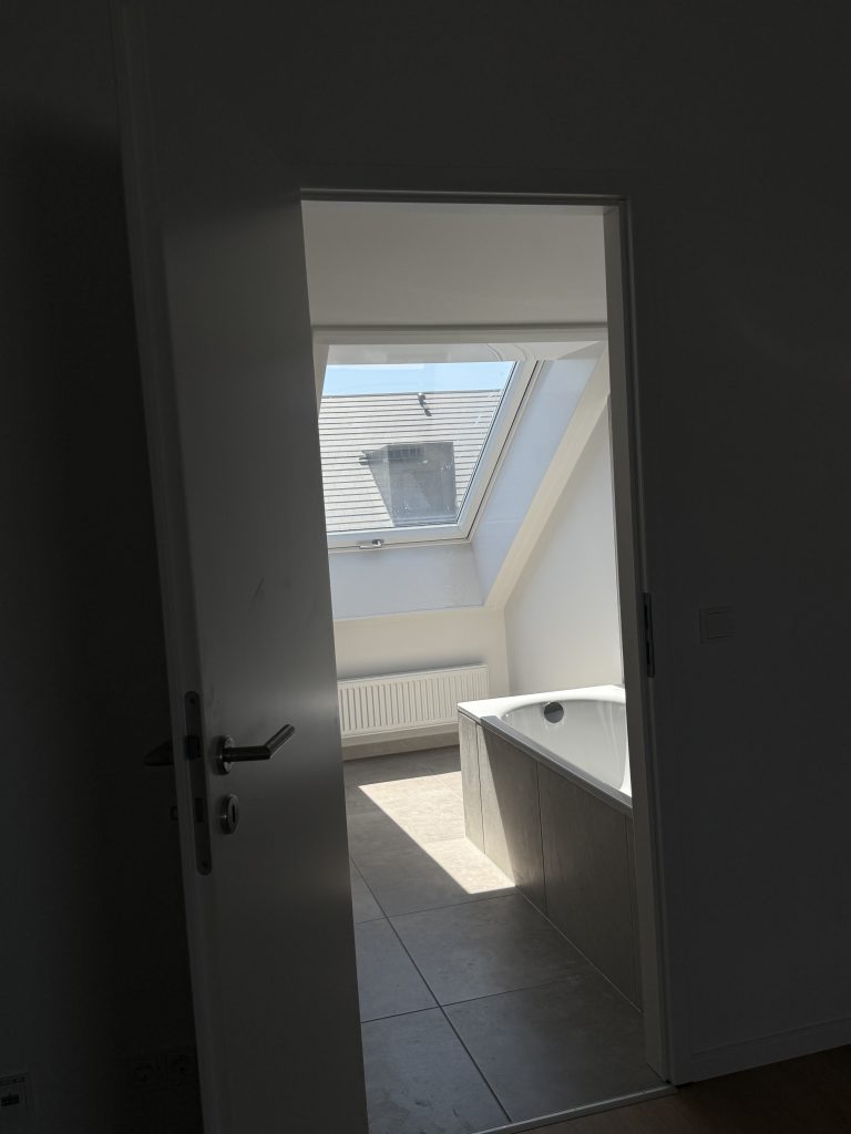 Dunkler Türrahmen mit Blick in ein helles Bad mit Dachfenster