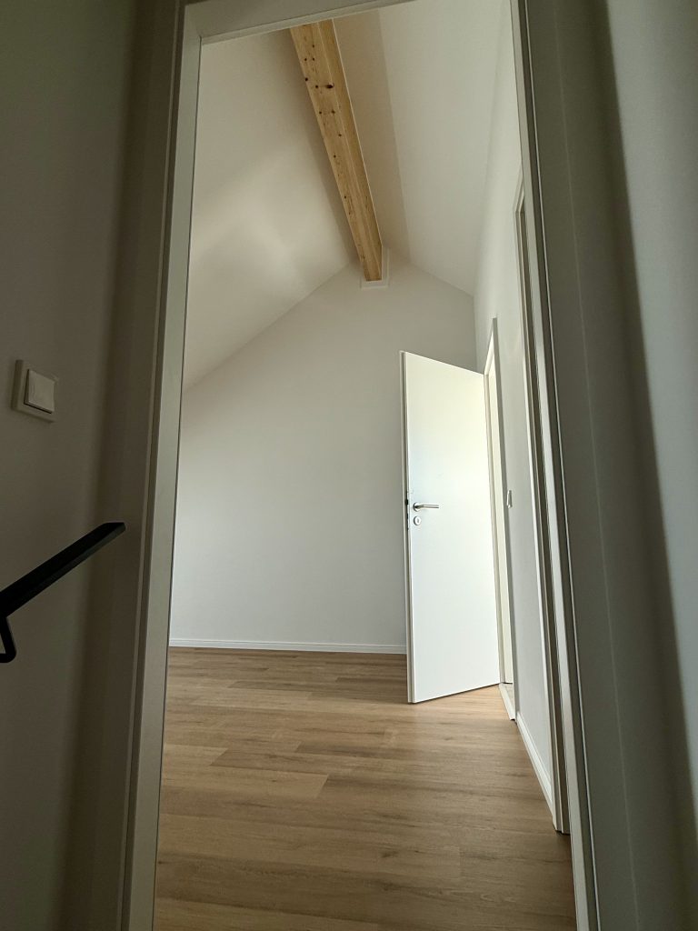 Blick durch eine Tür in ein Dachzimmer mit sichtbarem Holzbalken