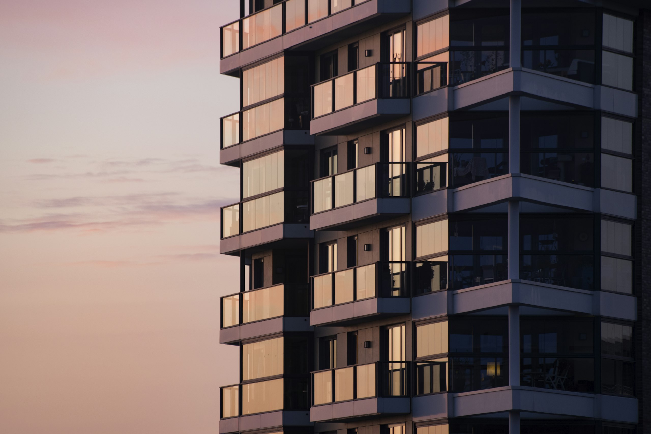 Ecke eines mehrgeschossigen Wohnhauses mit Balkonen im warmen Licht der Abenddämmerung