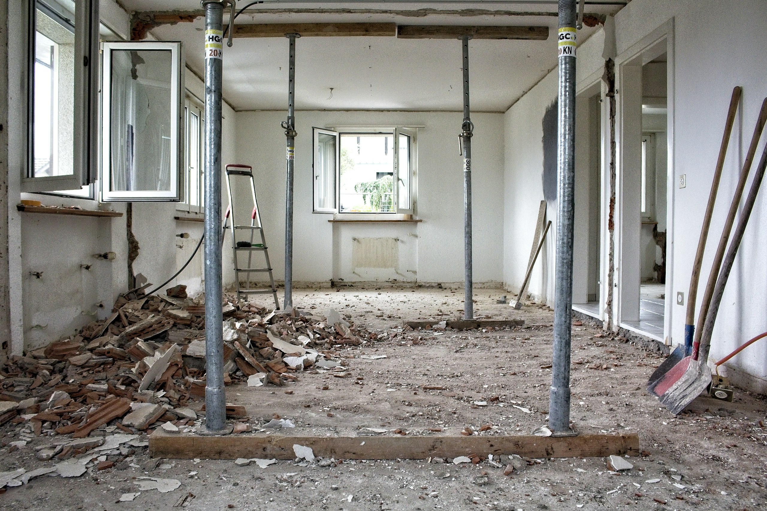 Entkernter Wohnraum mit Stahl-Deckenstützen, Bauschutt auf dem Boden und geöffneten Fenstern