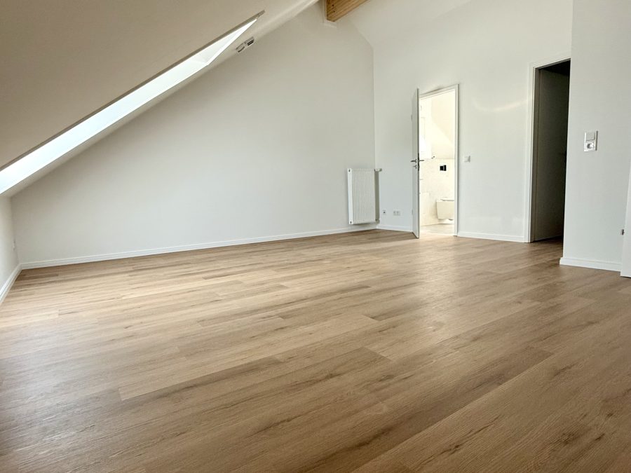 Großes leeres Dachzimmer mit Dachfenster, Holzbalken und Eichenboden