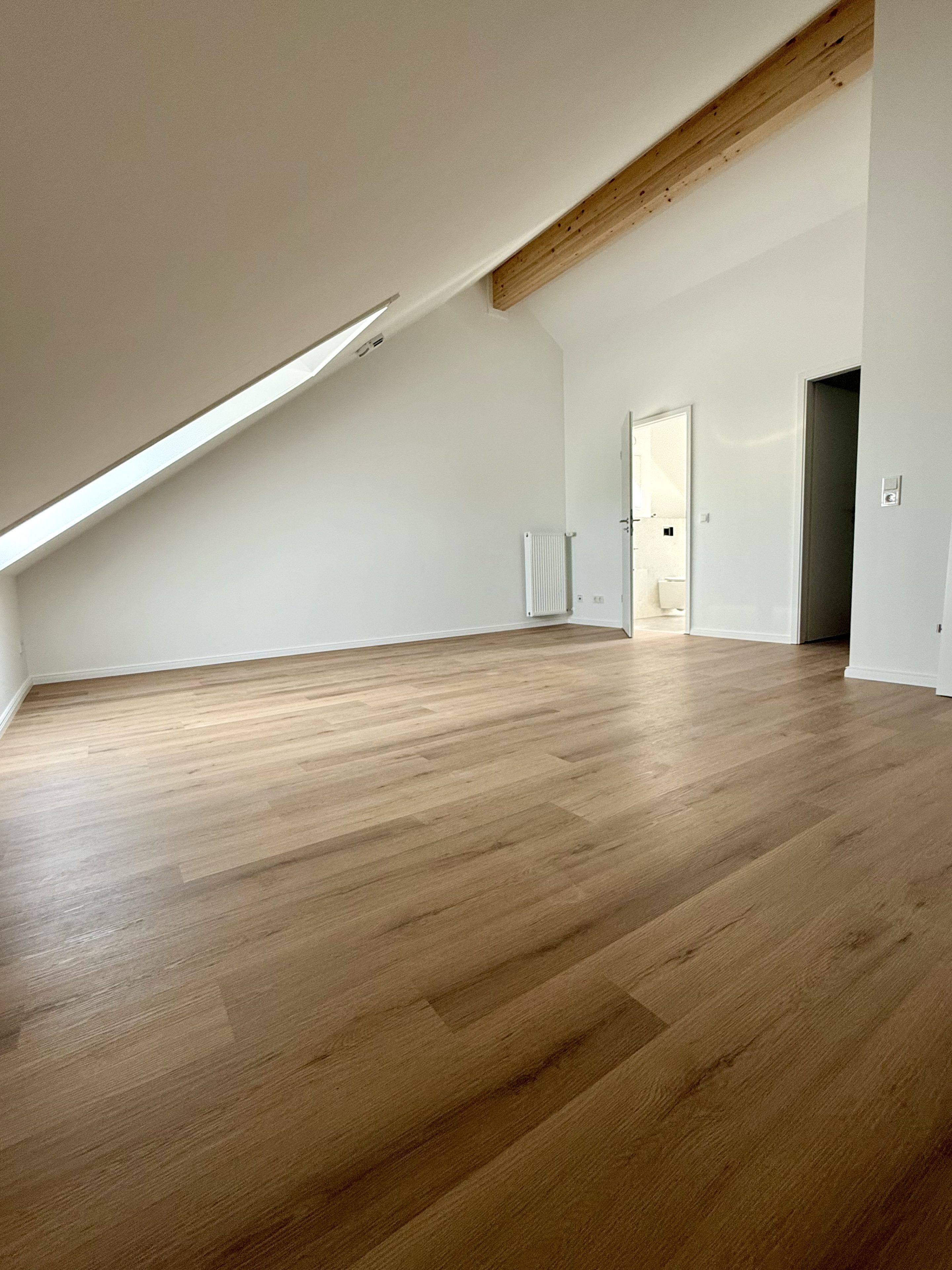 Großes leeres Dachzimmer mit Dachfenster, Holzbalken und Eichenboden