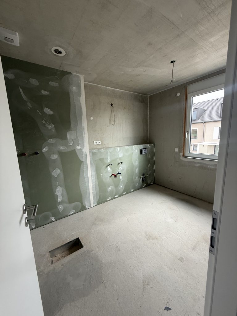 Badezimmer im Rohbau mit grünen Feuchtraumplatten und Rohranschlüssen