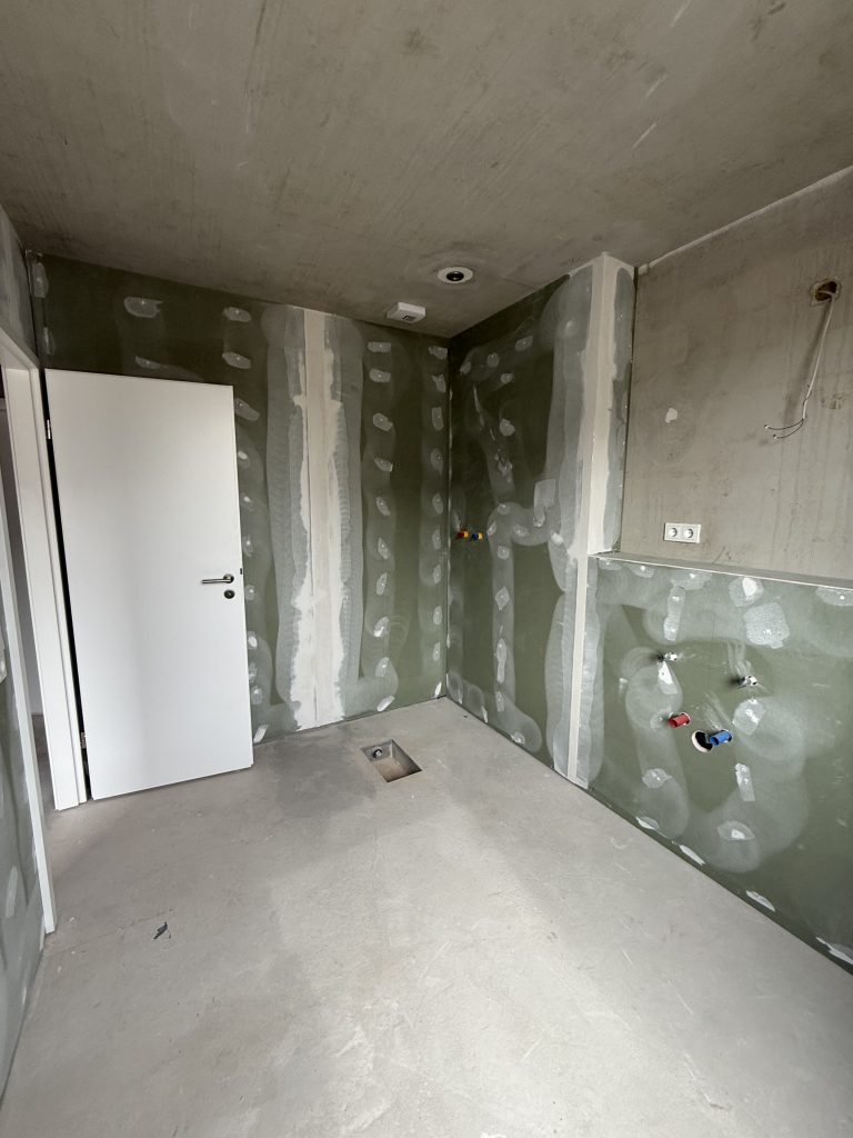 Duschecke im Rohbau mit grünen Feuchtraumplatten und Bodenablauf