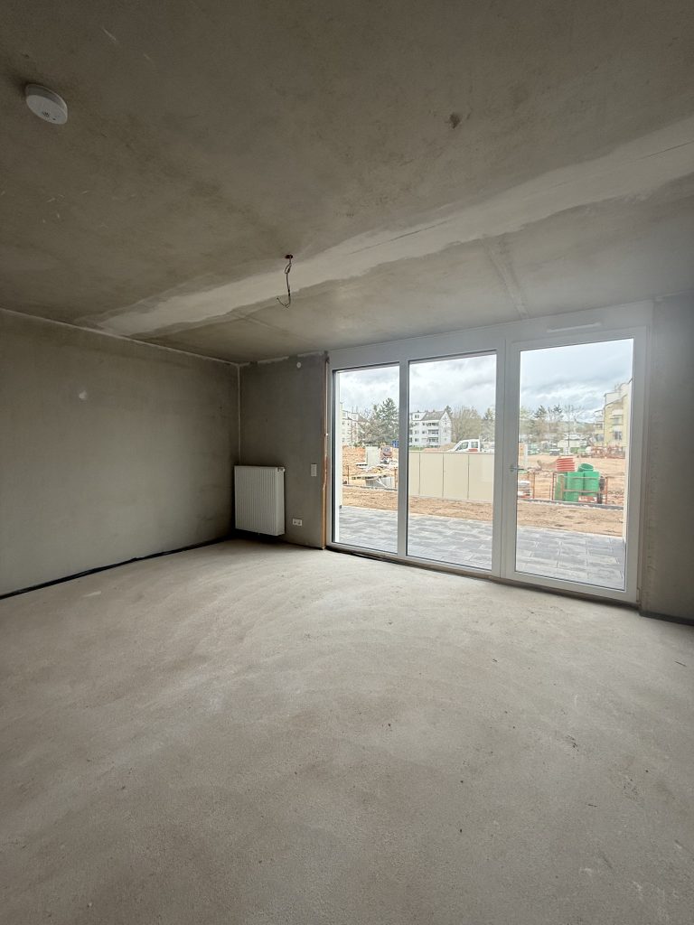 Wohnraum im Rohbau mit großer Terrassentür und Betondecke