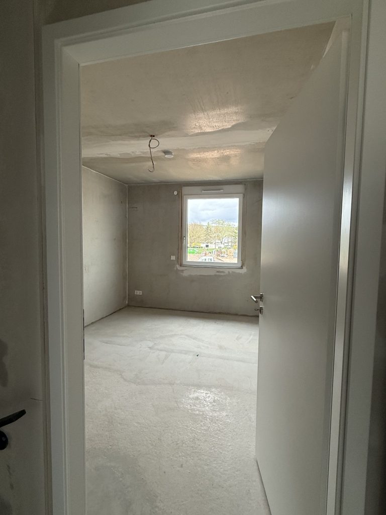 Blick durch eine offene Tür in ein Rohbauzimmer mit Fenster