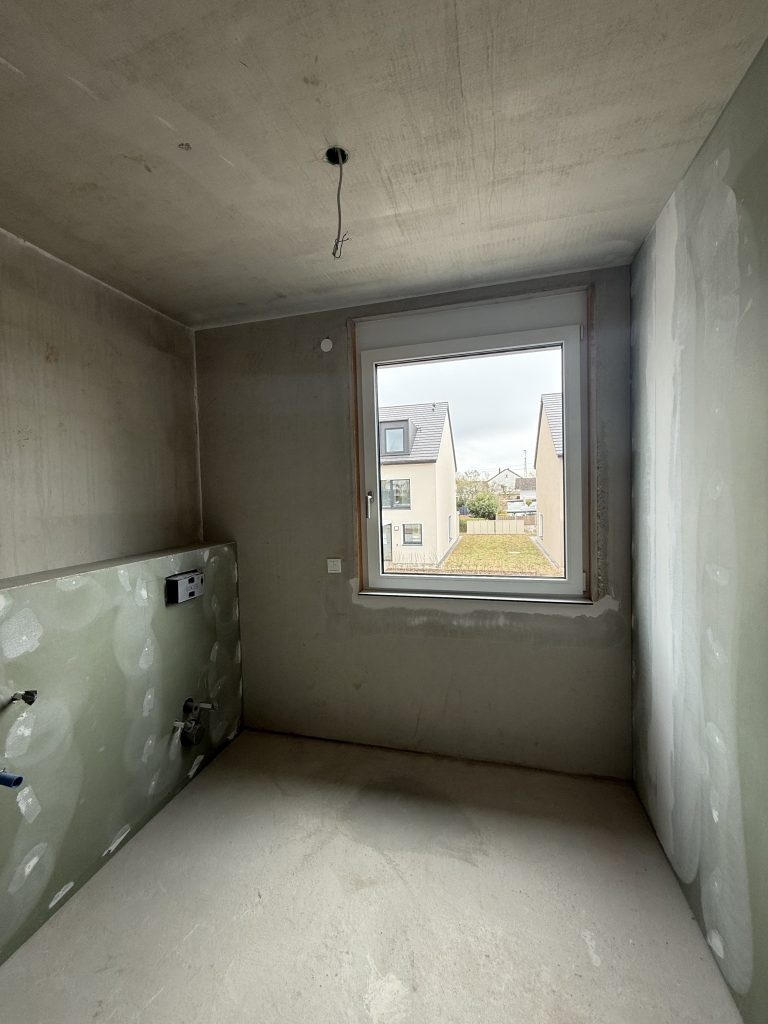 Rohbauzimmer mit Fenster und grüner Feuchtraumplatte mit Rohranschlüssen