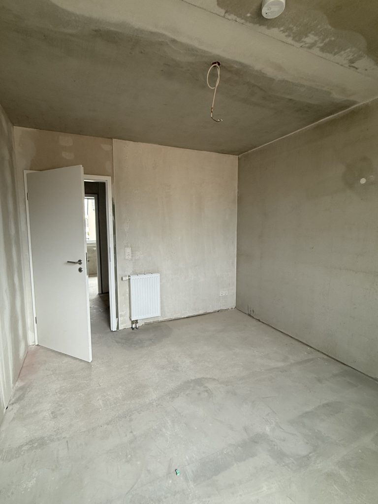 Zimmer im Rohbau mit Heizkörper und offener Tür zum Flur