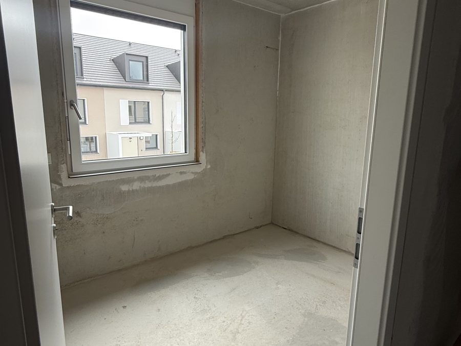 Kleines Rohbauzimmer mit Fenster, Betonwänden und Estrich