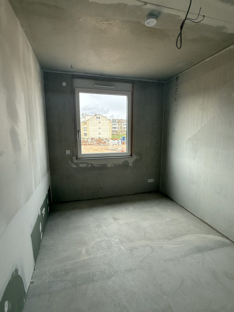 Zimmer im Rohbau mit Fenster und Blick auf die Baustelle