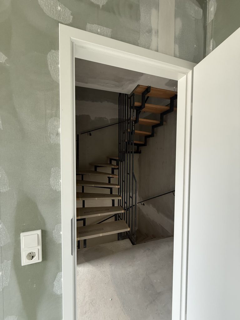 Blick durch eine Tür auf eine Treppe mit Stahlwange, Holzstufen und schwarzem Geländer